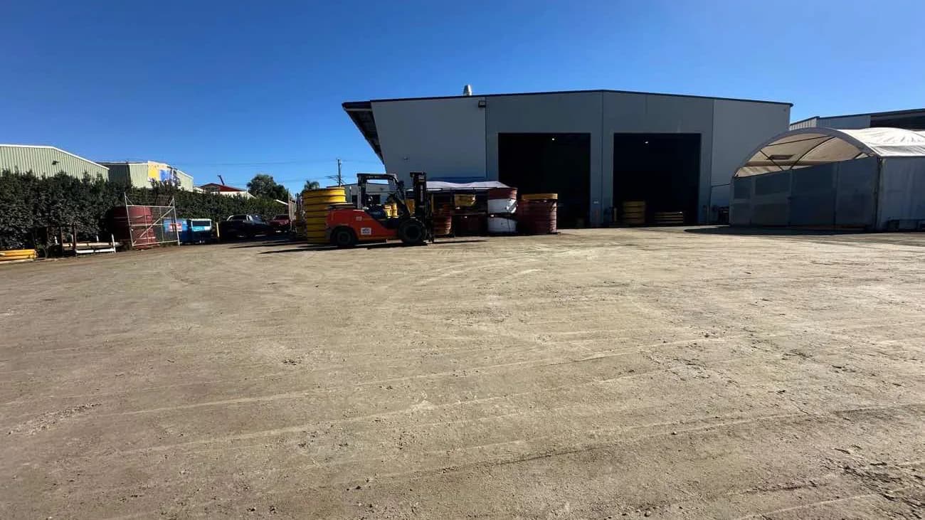 A level, bound hardstand yard in front of an industrial shed under a clear sky